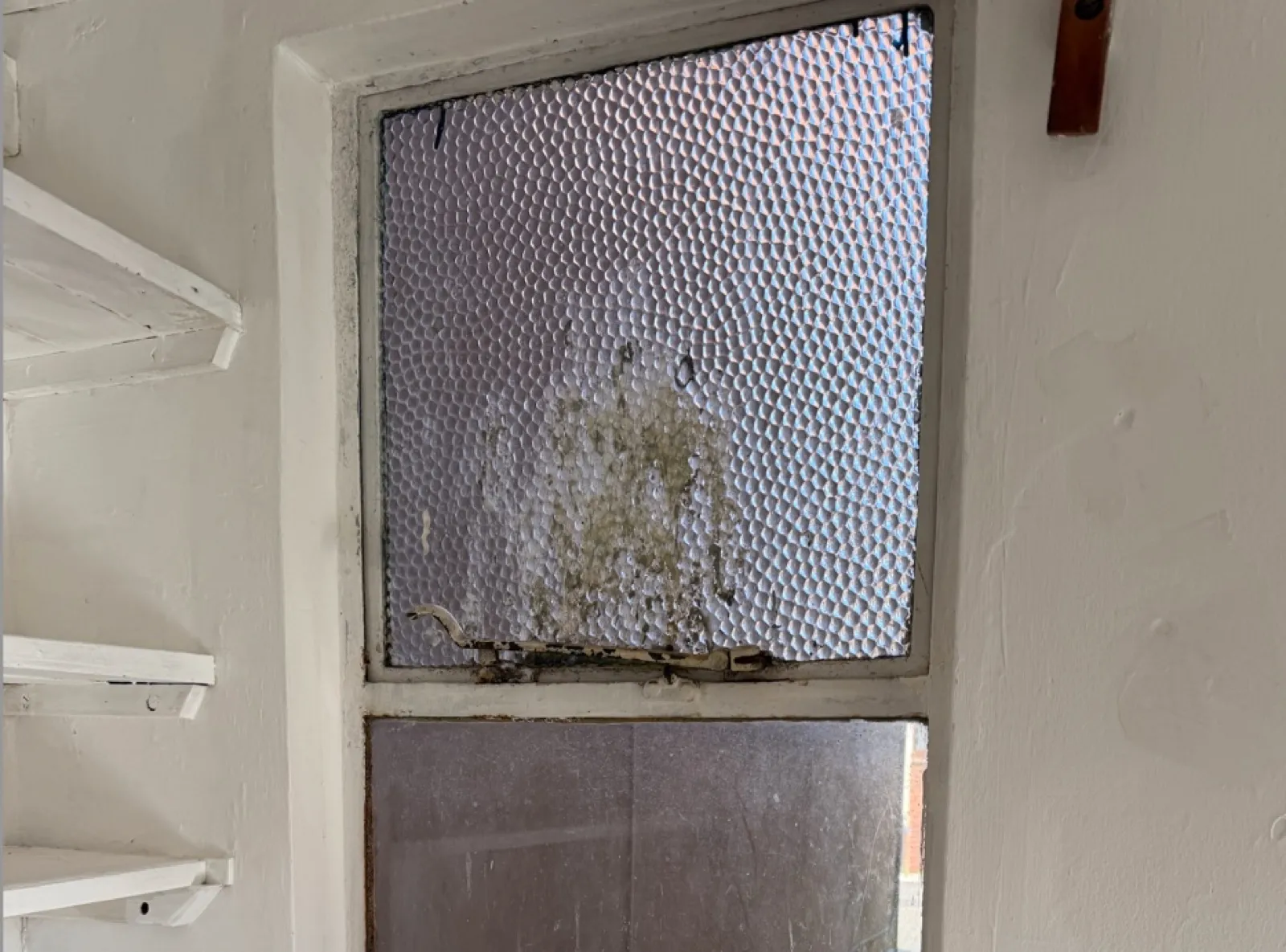 Original Crittall steel-framed window with reeded textured glass, showing significant rust at the bottom of the frame, condensation damage, and a corroded handle — typical of unrestored Crittall windows in pre-war Hertfordshire properties