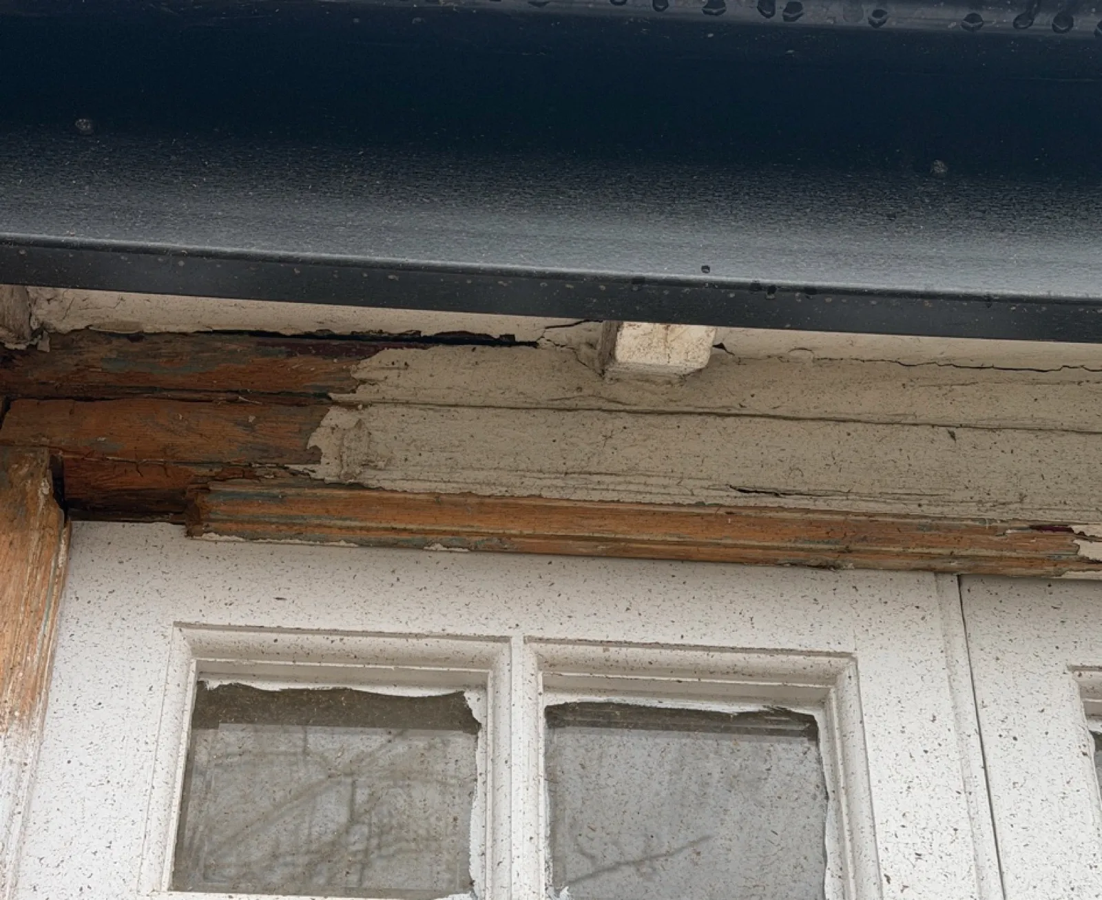 Severe rot in the timber lintel and head of a bay window, caused by water leaking from the roof and lead flashing above — paintwork has failed, the wood is splitting and exposed, and the damage extends across the full width of the bay