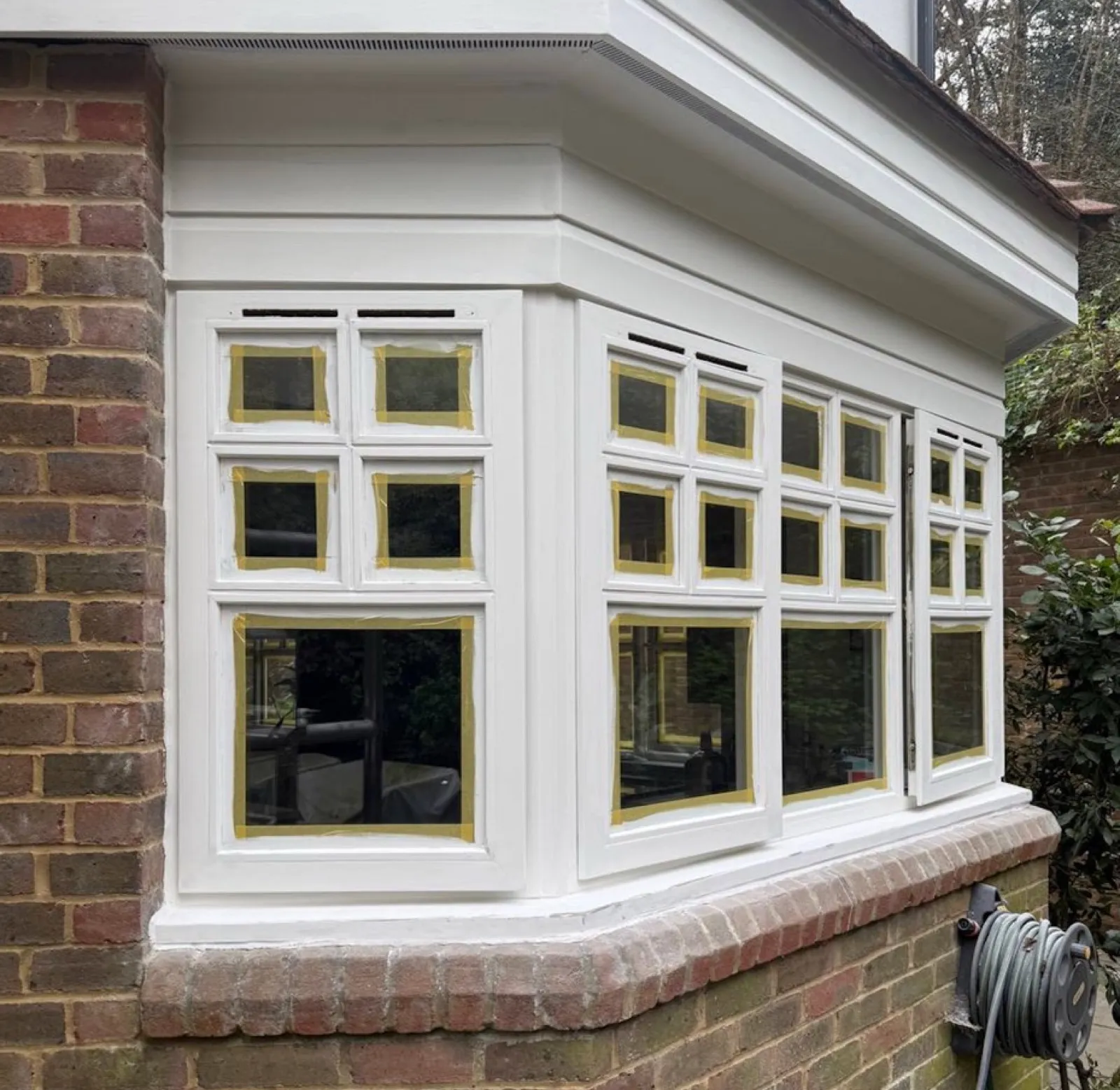 Bay windows in Hertfordshire mid-paint, with masking tape protecting the glass and a freshly applied coat of premium white exterior paint